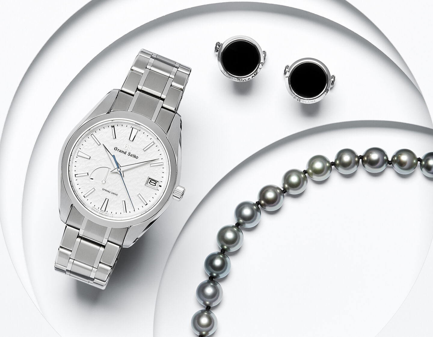 black cufflinks, a stainless steel watch, and black pearl necklace